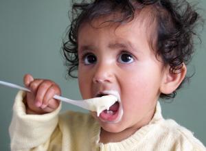 Baby eating food with a spoon.