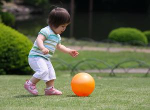 Little girl running and kicking ball in park.