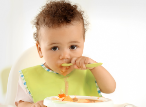 baby in highchair eating with spoon