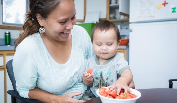 Mother with baby eating strawberries at a table.