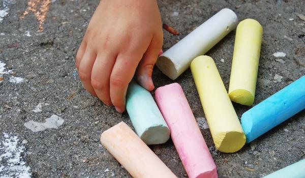 colourful chalk resting on the pavement. A child's hand reaching for one piece of chalk.