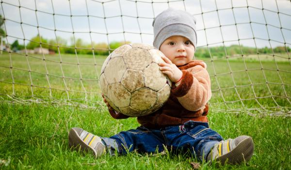 Child in front of net, holding a soccer ball.
