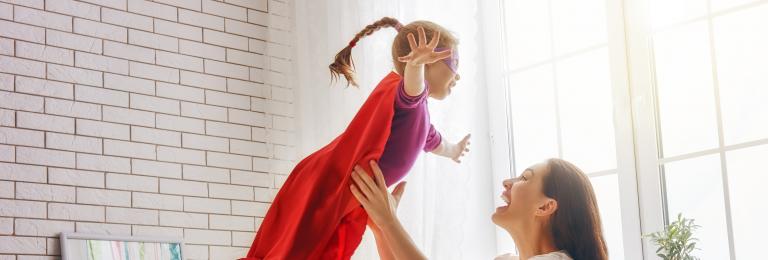 Girl with superhero cape jumping in to mothers arms