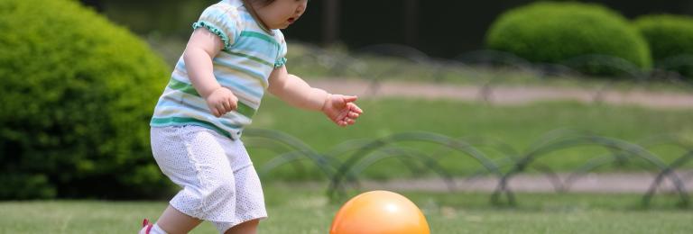 Little girl running and kicking ball in park.