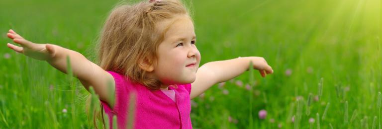 Child stretching out arms to the side, standing in grass.