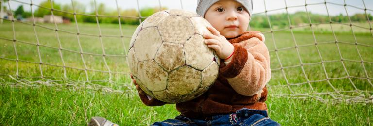 Child in front of net, holding a soccer ball.