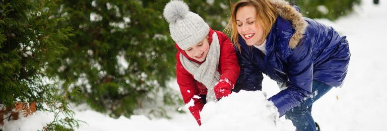 Child and caregiver making a snow boulder.