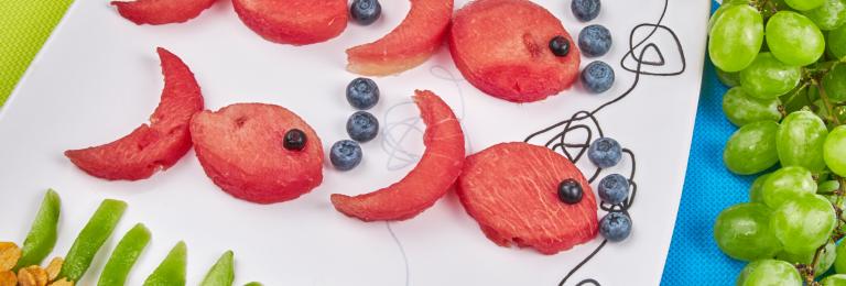 Fish made out of fruit on a white plate.